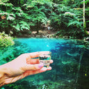 Ștefan cel Mare Moment: Hand holding a small glass of vodka with a scenic background of a blue pond and green trees.