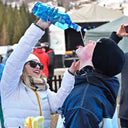 My Voronskaya Moment: Two people outdoors, one pouring a blue bottle into another's mouth, with a crowd in the background.