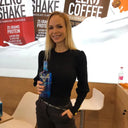 My Voronskaya Moment: Woman holding a blue bottle in front of promotional signs for protein shakes and coffee.